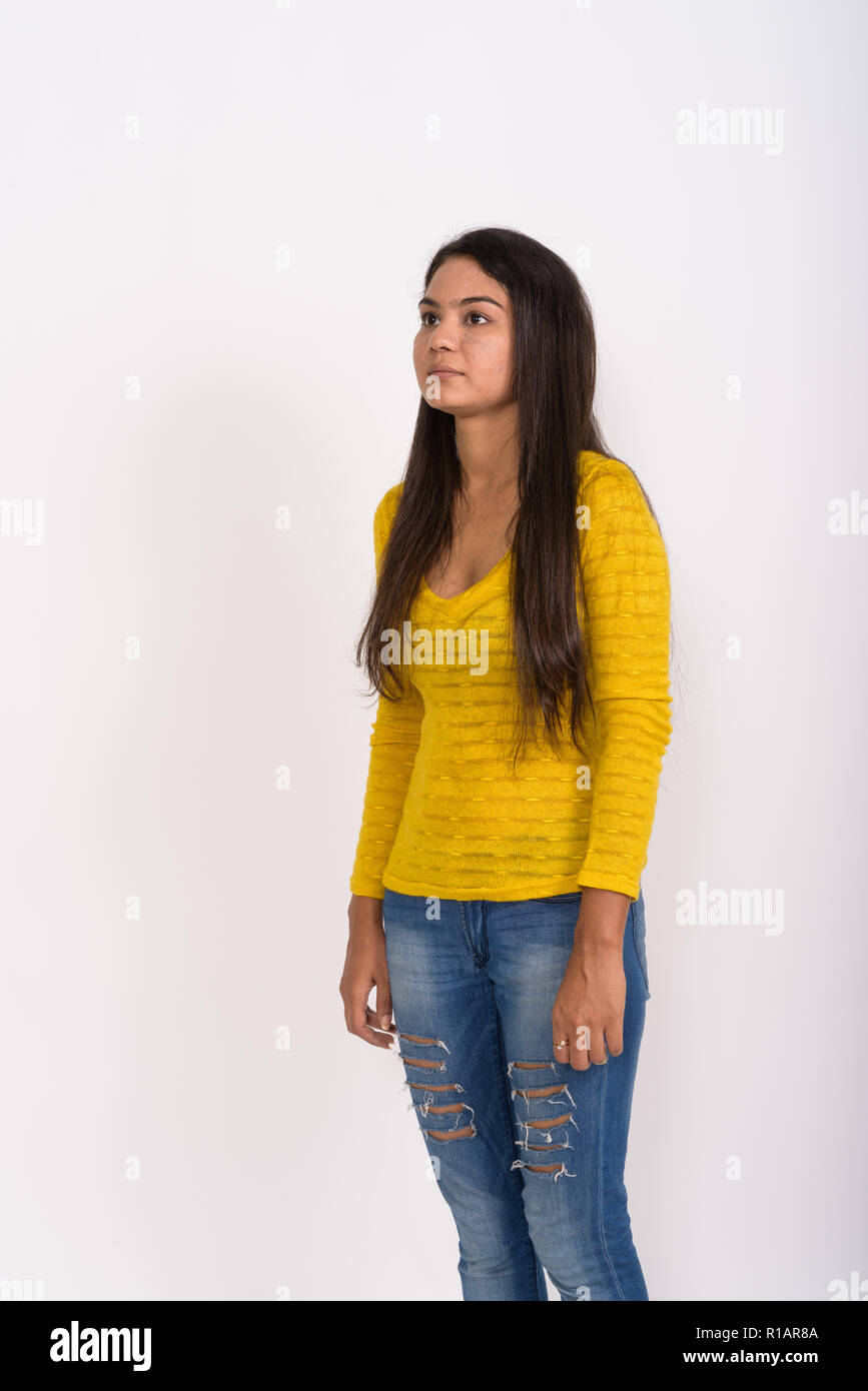 Studio shot of young Indian woman standing while thinking agains Stock Photo
