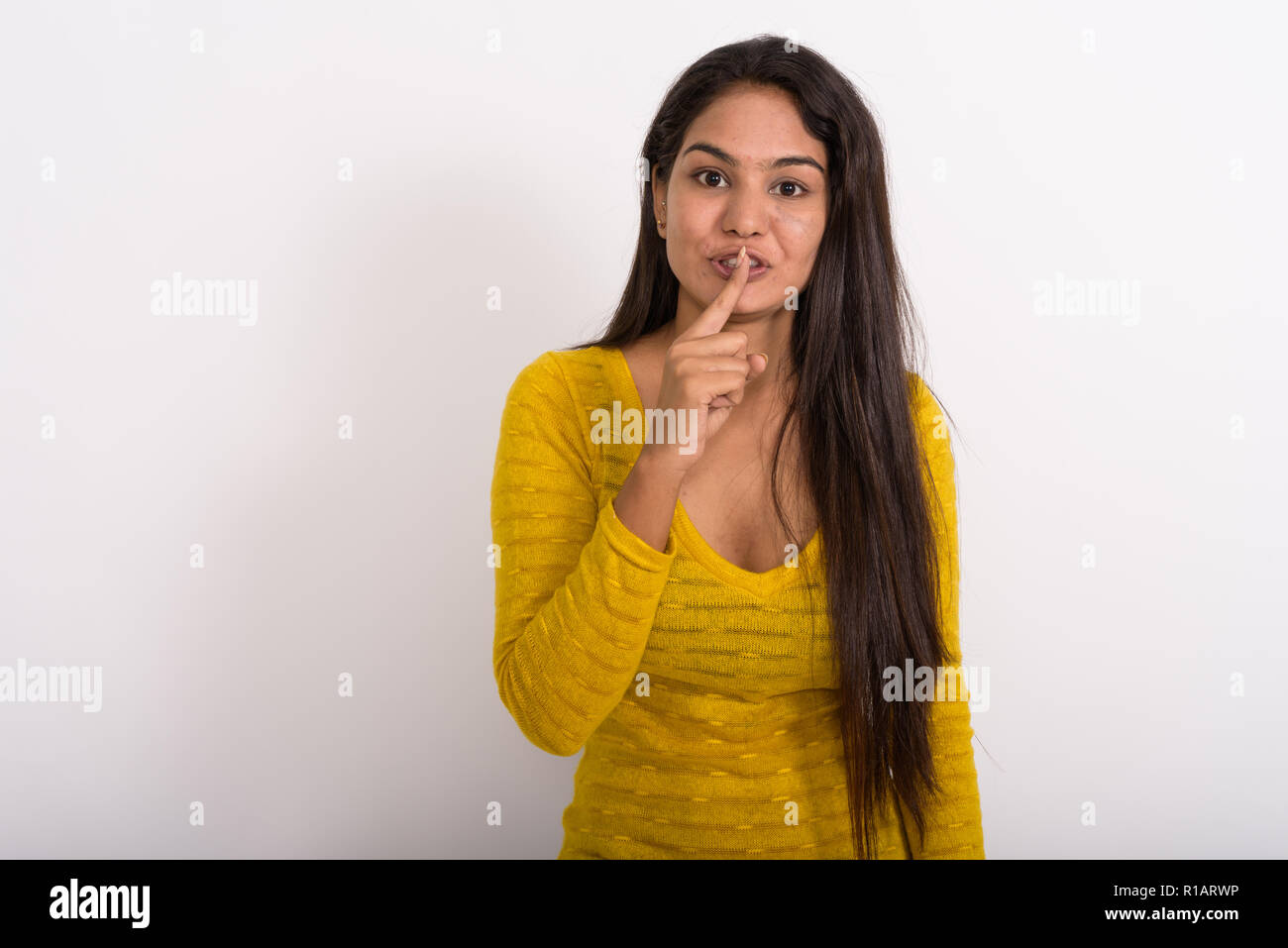 Studio shot of young Indian woman with finger on lips against wh Stock Photo