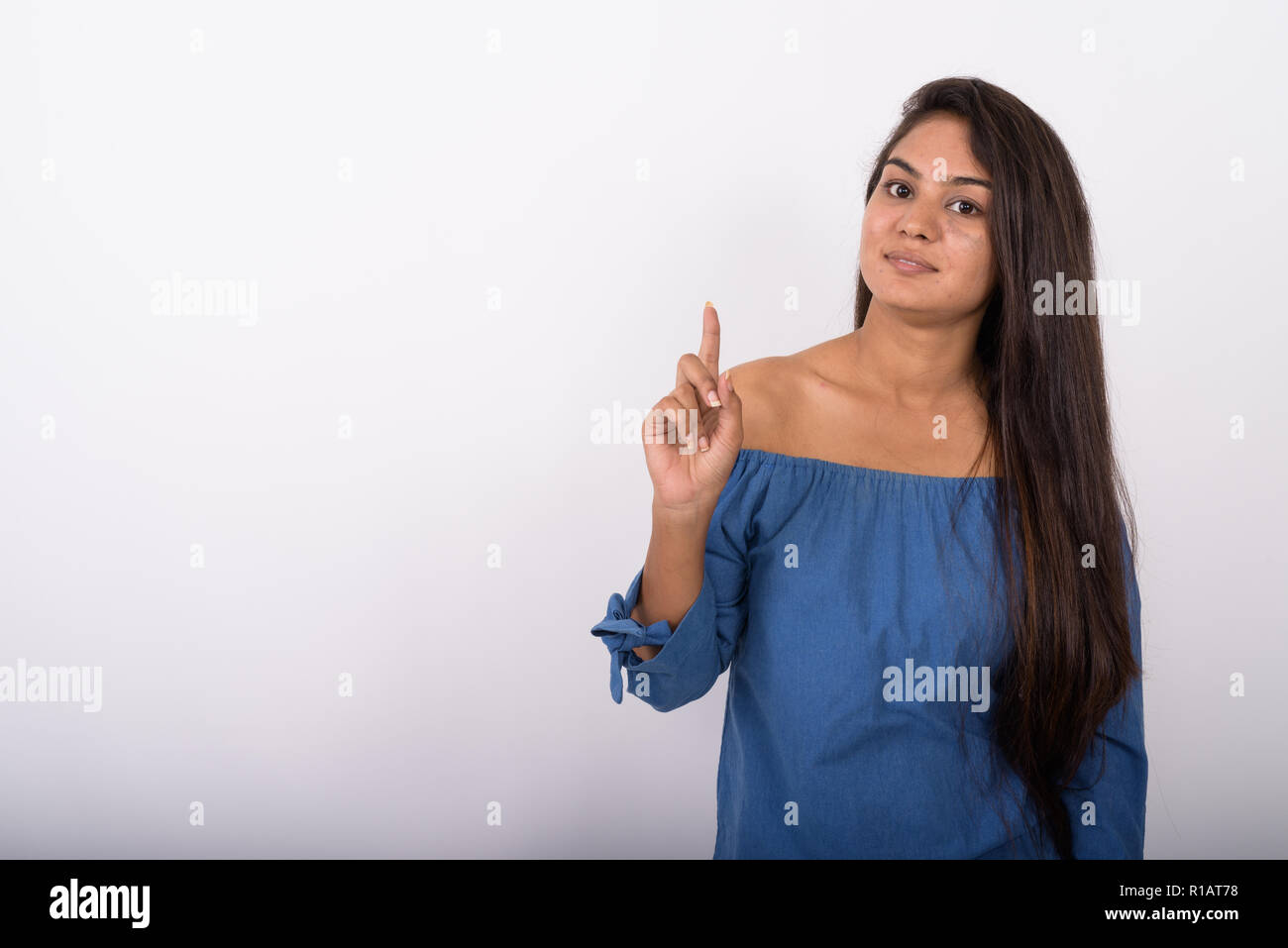 Studio shot of young Indian woman pointing finger up against whi Stock Photo