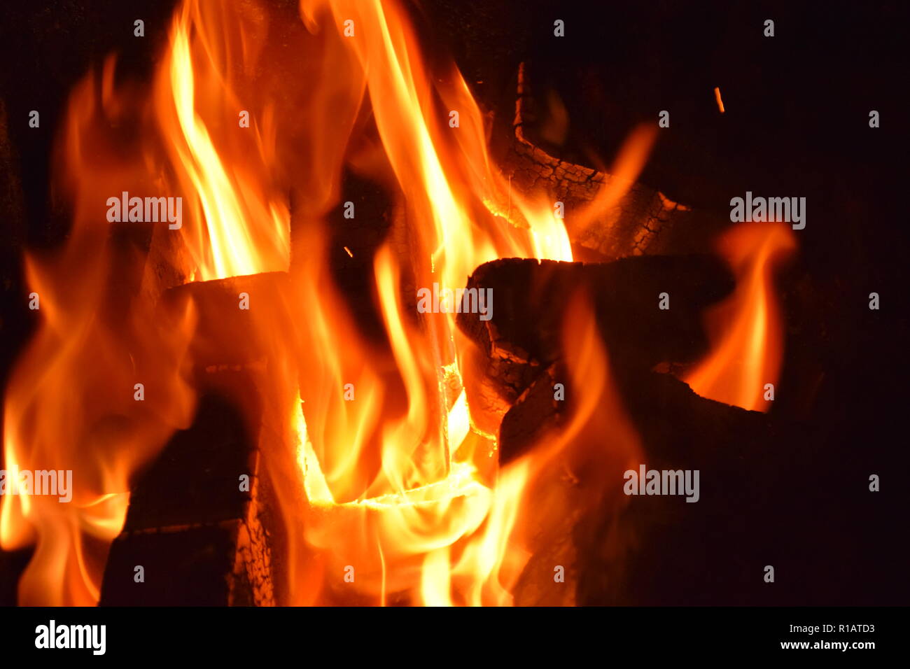 Close up of Brown Coal Briquettes on fire with red yellow flames inside a special solid furnace, red and orange blurry texture on a black background. Stock Photo