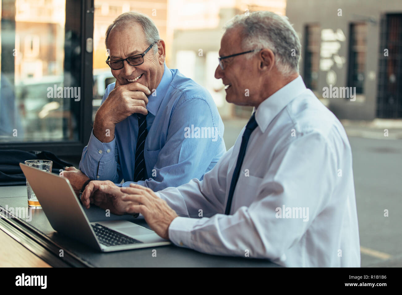 Senior businessmen at cafe with laptop discussing work and smiling. Senior business professionals having casual discussing over work at cafe after wor Stock Photo
