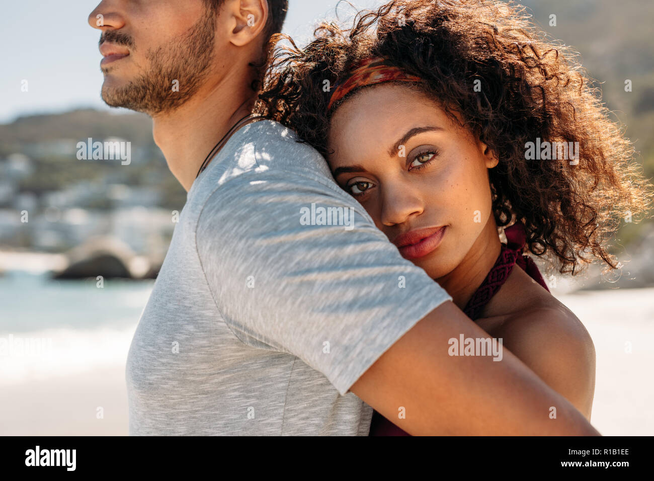 Side view of a couple in love standing outdoors. Woman holding her boyfriend from behind hugging him. Stock Photo