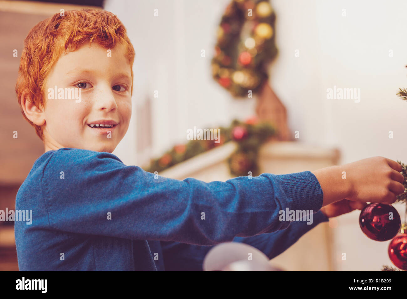 Cheerful preteen boy putting decorations on Christmas tree Stock Photo