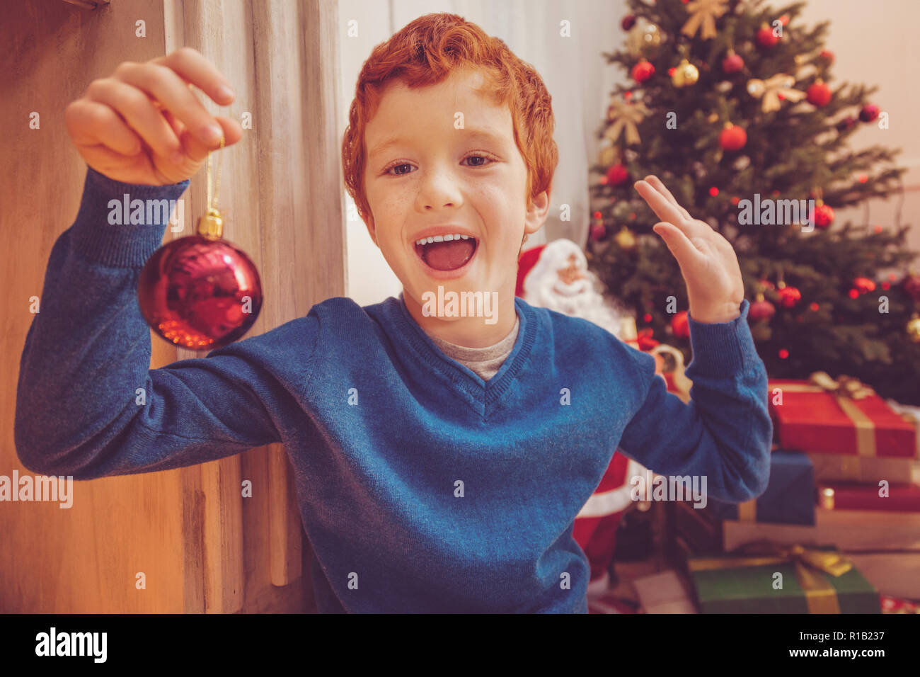 Cheerful ginger-haired boy showing new Christmas bauble Stock Photo
