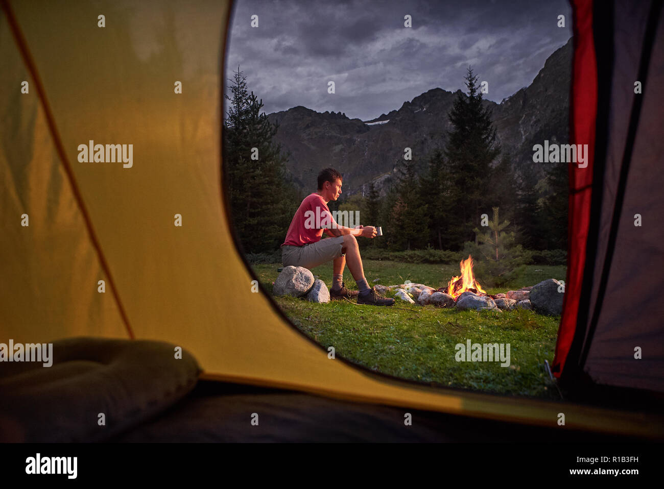 View from inside tourist tent at sunset. Alone tourist, man hiker sitting at bonfire Stock Photo