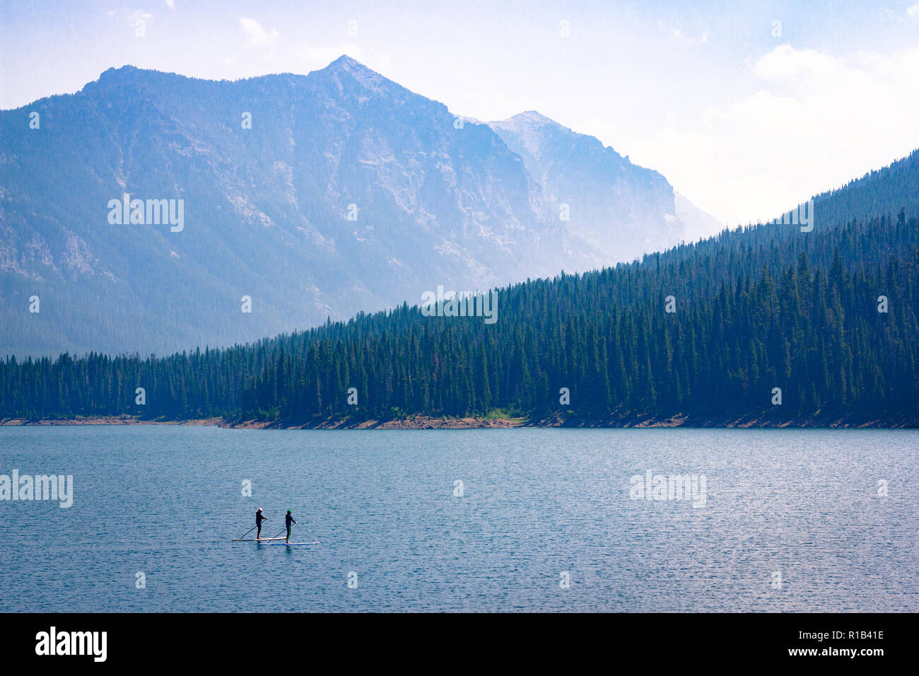 Mountain Lake Recreation. Paddle boarders drift through the Hyalite Reservoir in Montana. Relaxing outdoors vacation scene with majestic copy space. Stock Photo