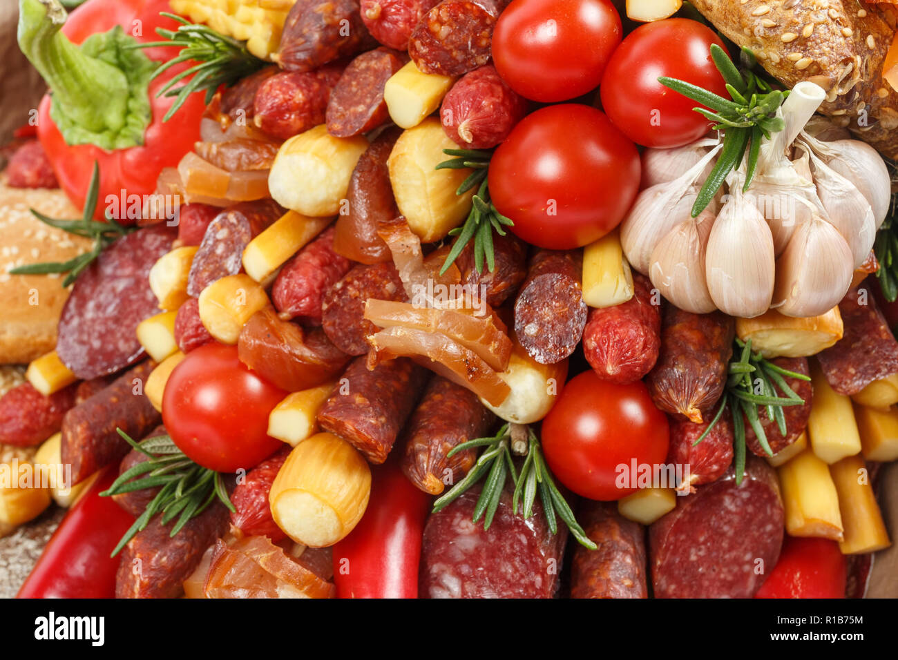 Set consisting of different varieties of sausage, meat, smoked cheese, tomatoes, pepper and bread as background Stock Photo