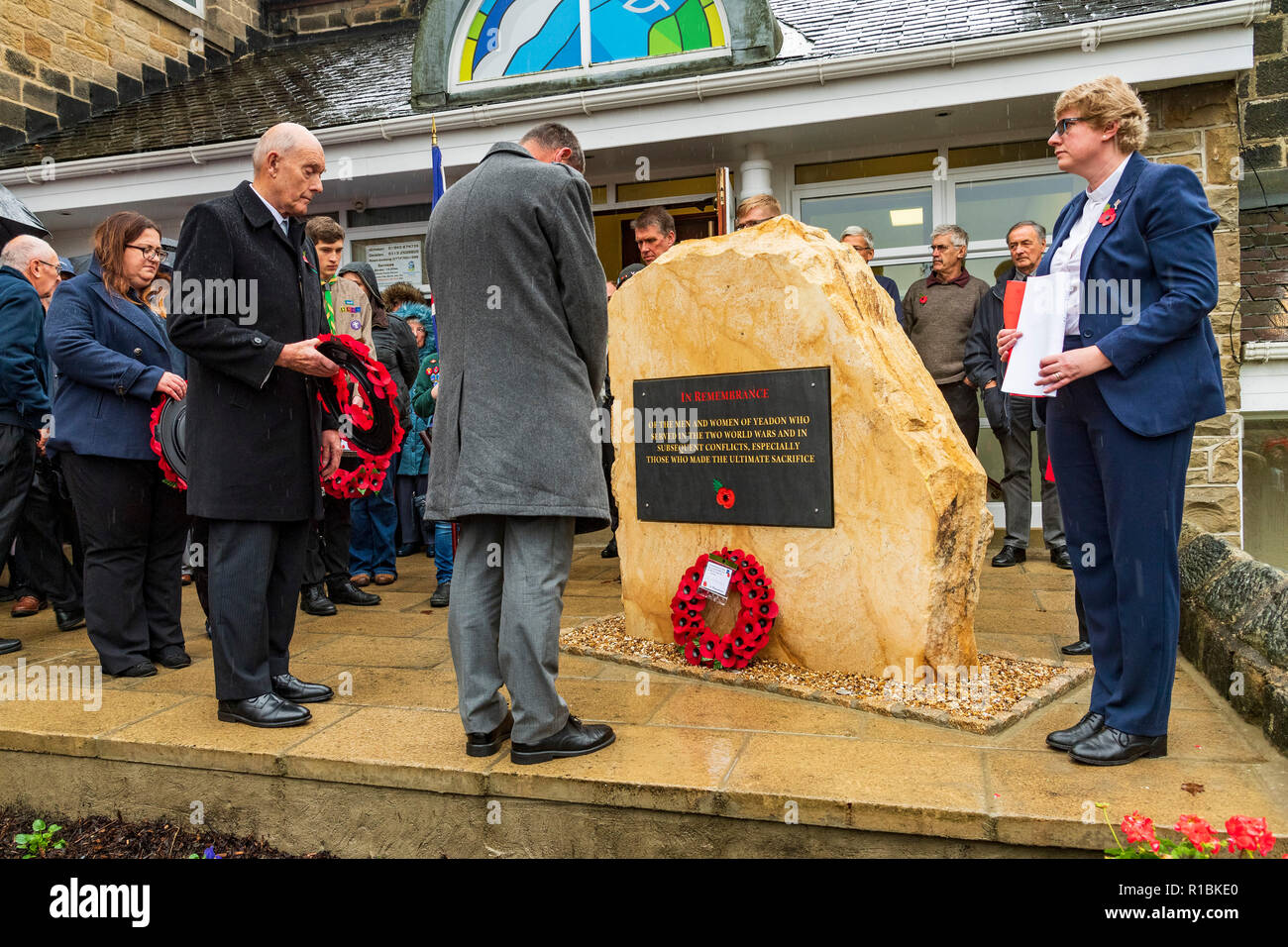 Yeadon, Leeds, West Yorkshire, UK 11th November, 2018. People are gathered round the new war memorial stone in front of Yeadon Methodist Church for a service of dedication & remembrance. The first poppy wreath has been laid and a man is bowing his head in respect. Ian Lamond/Alamy Live News. Stock Photo