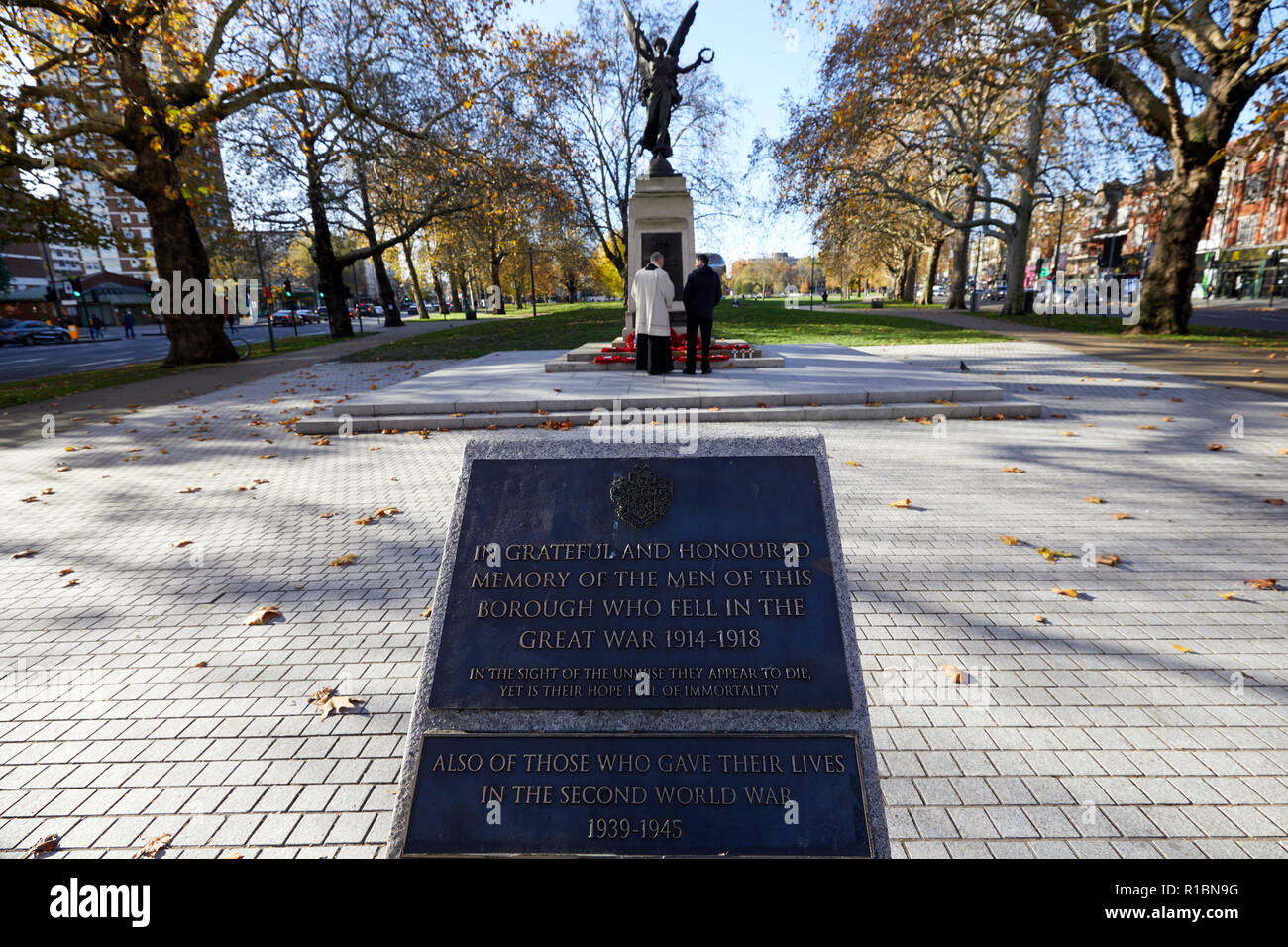London, UK. - 11 November 2018: A man along with a local vicar reflect at the Hammersmith War Memorial on Shepherd's Bush Green on the 100th anniversary since the end of World War One. Credit: Kevin J. Frost/Alamy Live News Stock Photo
