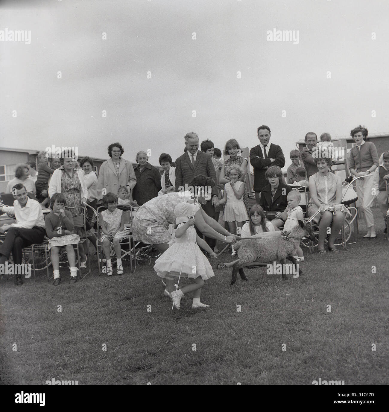 1967, historical, at an English village summer fete, a mother and her daughter dressed as 'little bo-peep', a character from a popular children's nursery rhyme about a shepherdess, running in a field holding small sheep or lamb, England, UK. Stock Photo