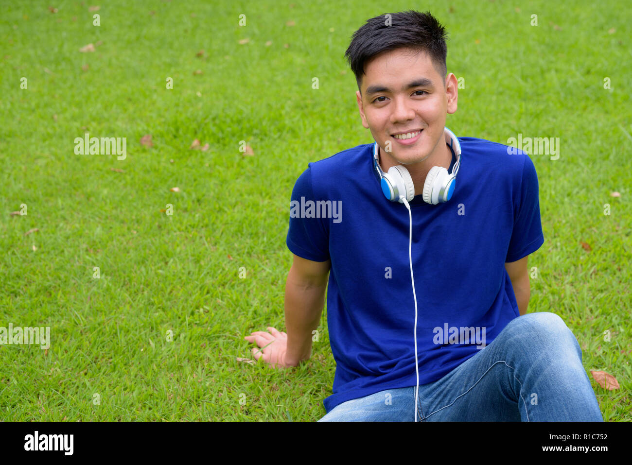 Young handsome Asian man relaxing at the park with headphones Stock Photo