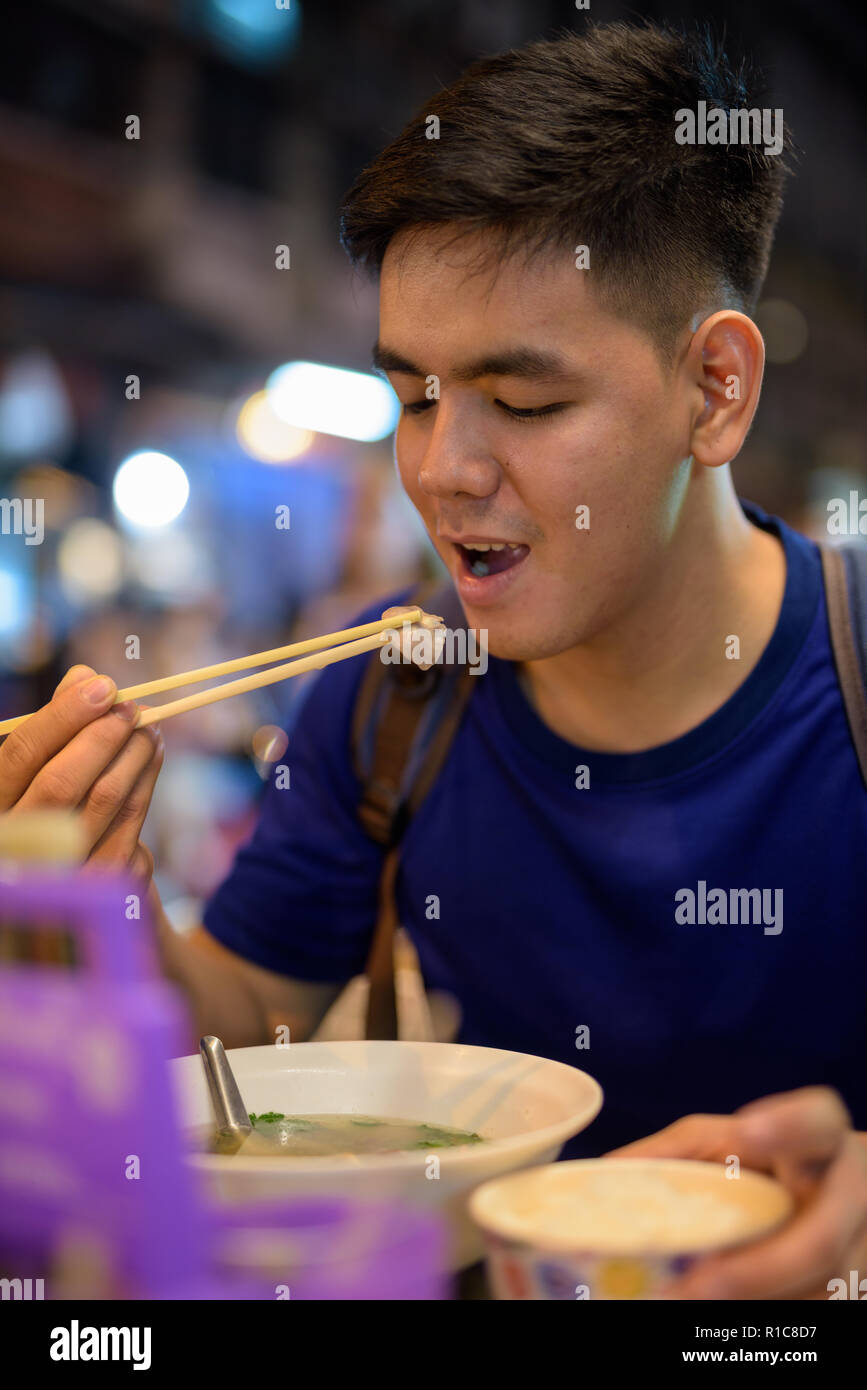 Young Asian tourist man exploring at Chinatown while eating noodle soup Stock Photo