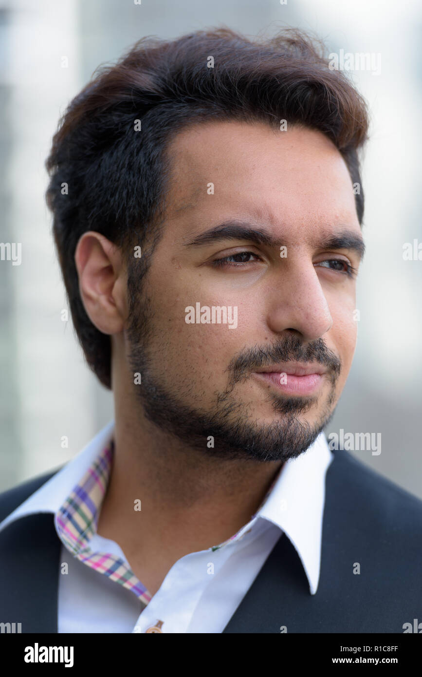 Face of young handsome Indian man thinking outdoors in the city Stock Photo