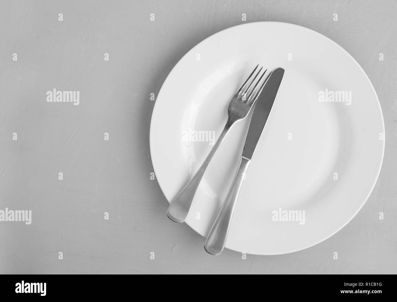 Knife and fork on white plate isolated on grey background with copy space - top view photograph Stock Photo