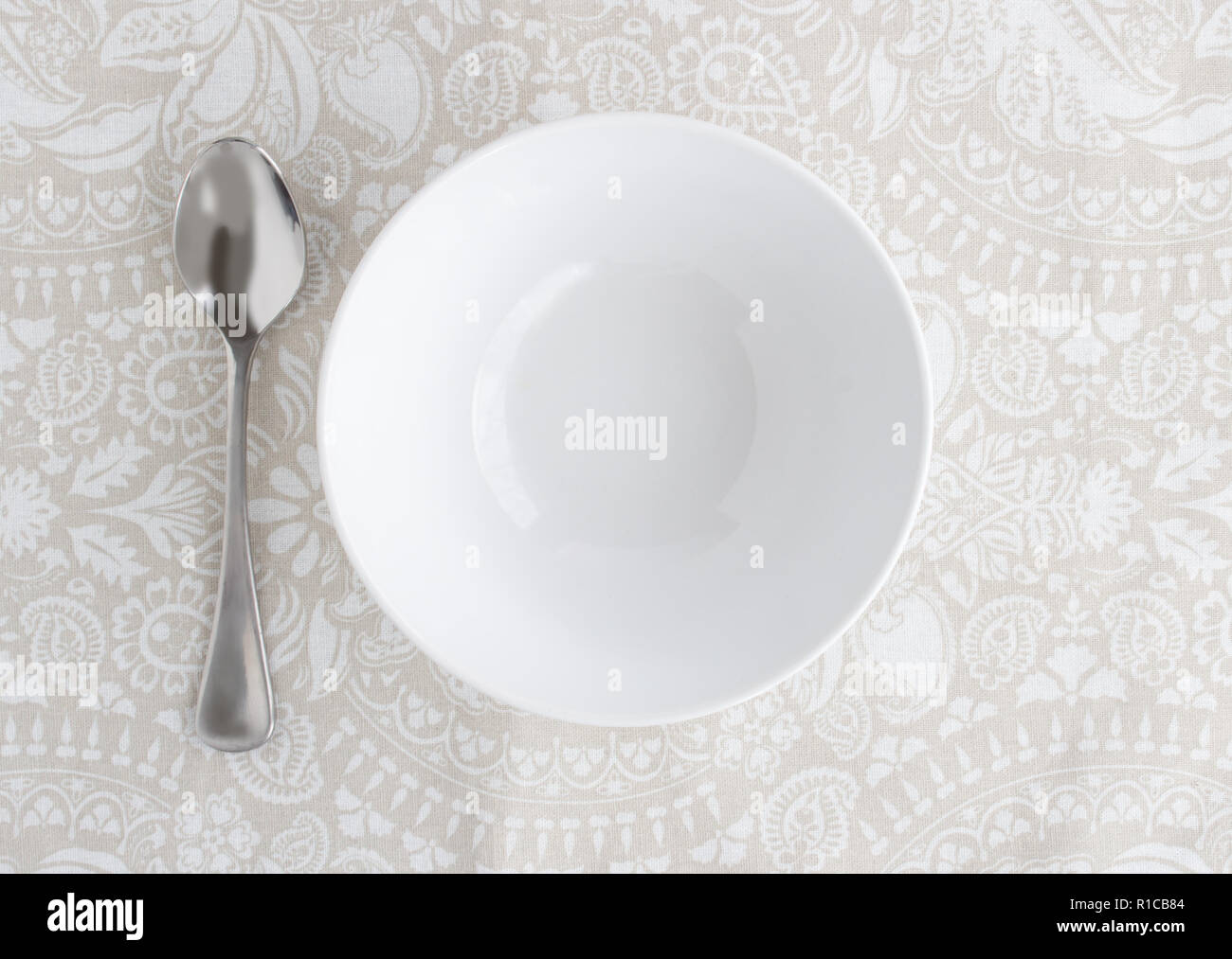 Bowl and silver spoon empty on patterned table cloth - Top view photo Stock Photo