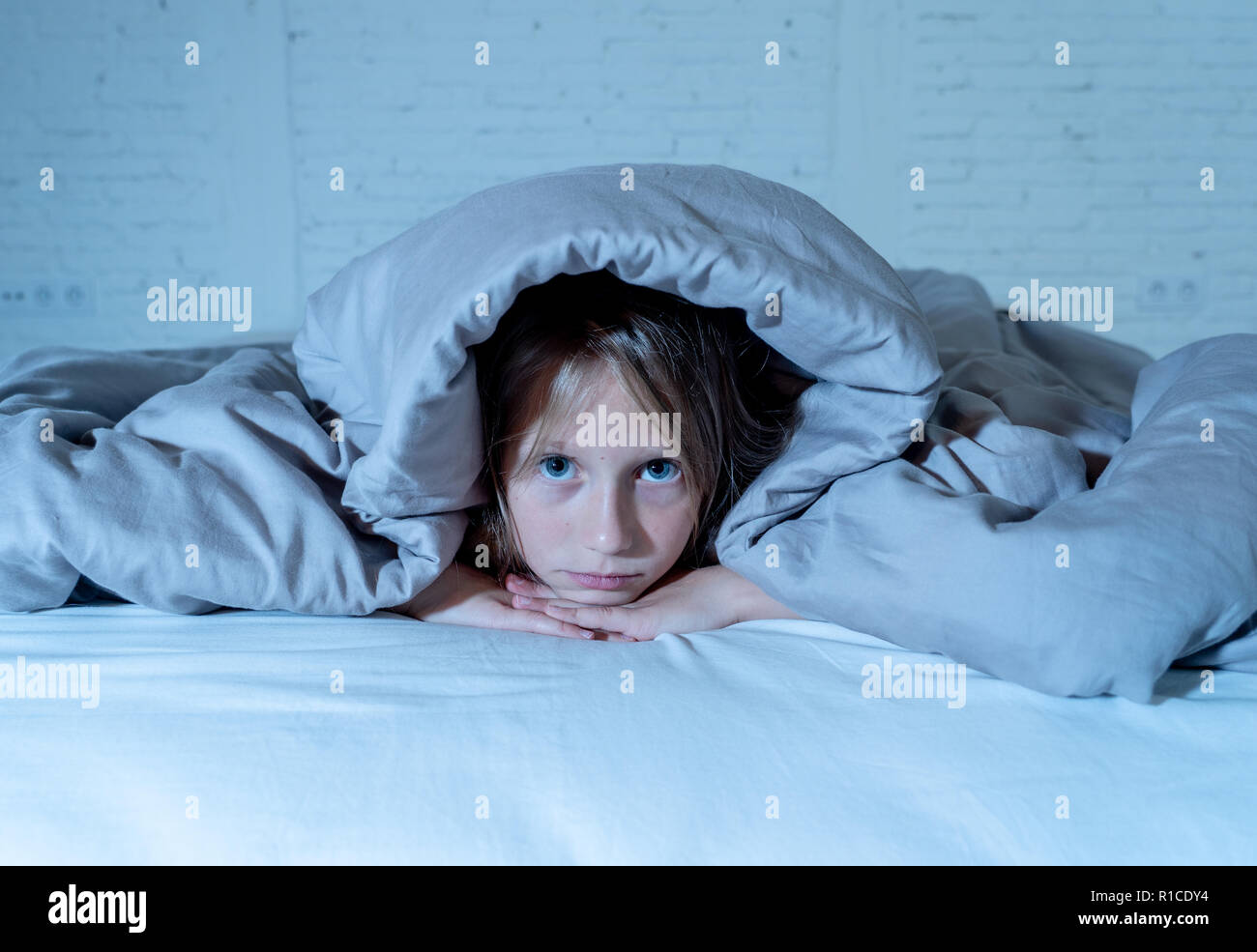 Cute little caucasian girl lying in bed covering her head with blanket