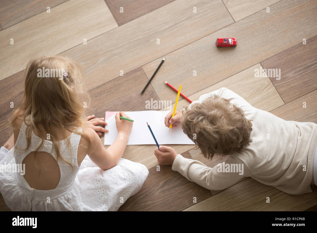 Brother and sister drawing with pencils on sheet in room Stock Photo