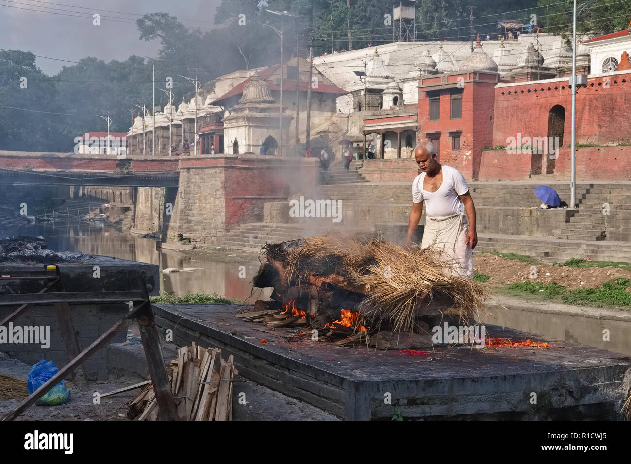 A man of the Dom caste traditionally employed to cremate dead bodies conducts a cremation at Pashupatinath Temple, Kathmandu, Nepal Stock Photo