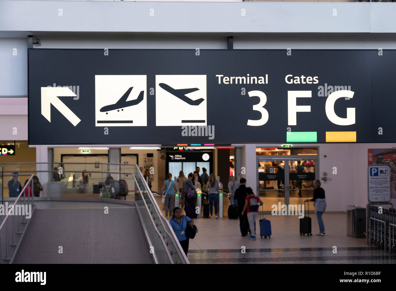 An illuminated sign at Vienna International Airport showing directions for arrivals, departures and gates, Passengers with suitcases. Austria Stock Photo