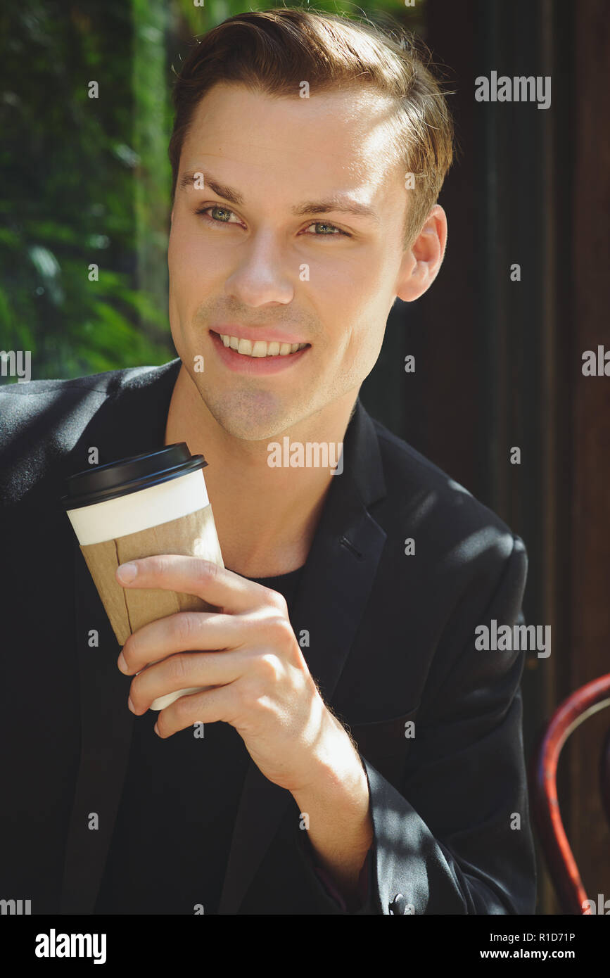 A businessman close-up portrait. He is smiling and holding a coffee cup in his hand. An outdoor portrait of an optimistic young entrepreneur. Stock Photo