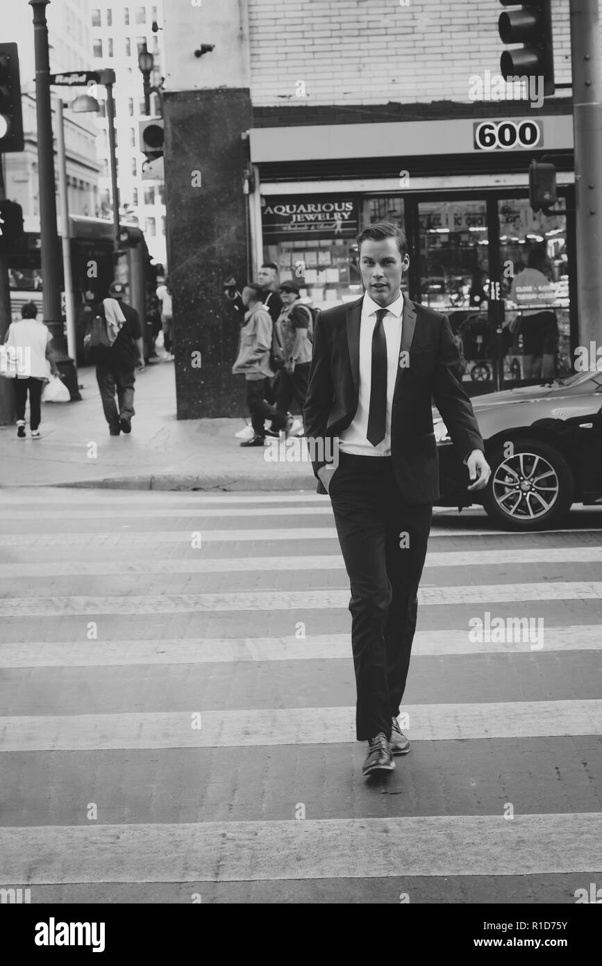 A black and white portrait of a male model walking on the streets of downtown Los Angeles. He is handsome and well dressed in a black suit and tie. Stock Photo
