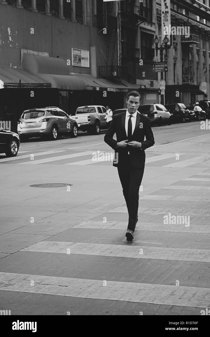 A black and white portrait of a male model walking on the streets of downtown Los Angeles. He is handsome and well dressed in a black suit and tie. Stock Photo