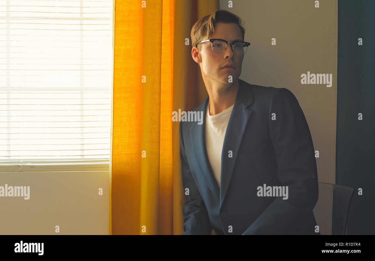 A young man, male model in blue suit and white pants,wears a pair of vintage glasses, looking away. A men's vintage editorial concept Stock Photo