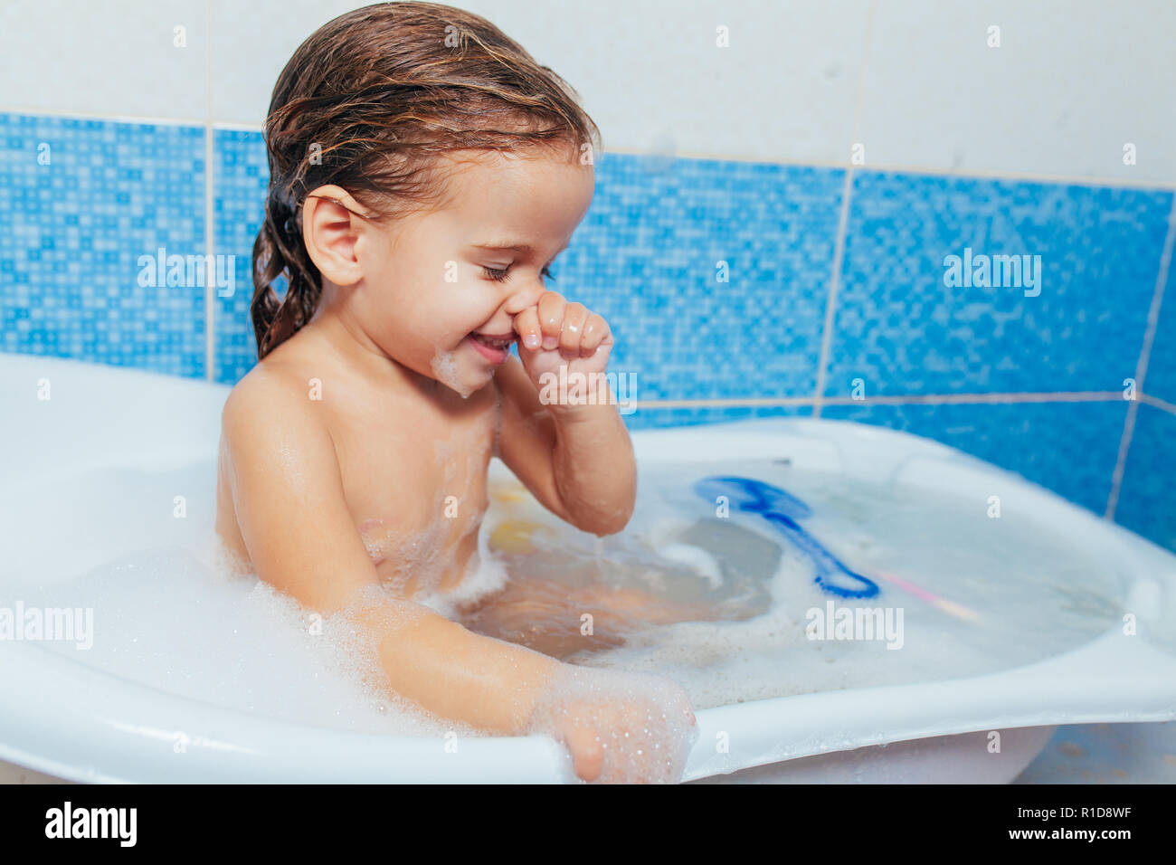 Fun cheerful happy toddler baby taking a bath playing with foam bubbles