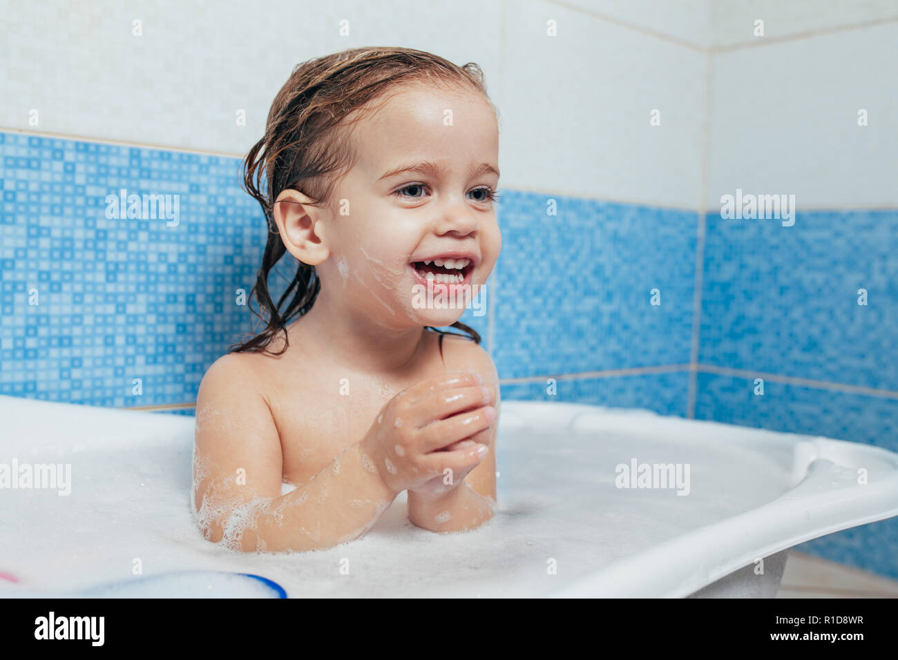Fun cheerful happy toddler baby taking a bath playing with foam bubbles