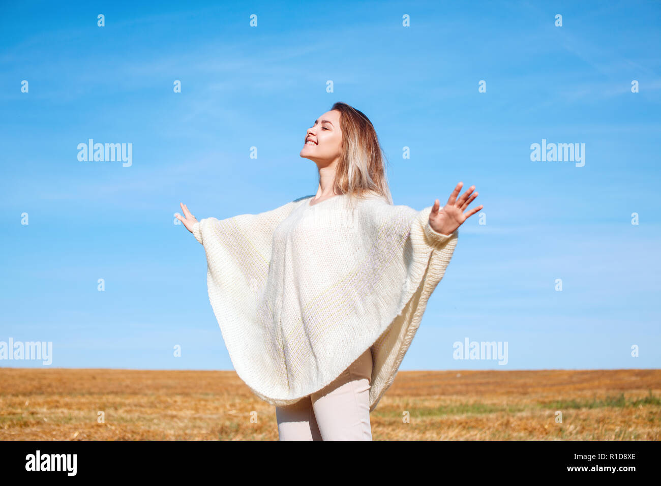 Cheerful girl with raised hands on the field in warm autumn season. Stock Photo