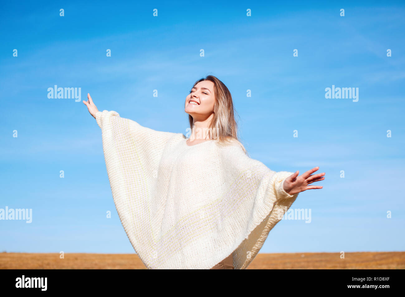 Cheerful girl with raised hands on the field in warm autumn season. Stock Photo