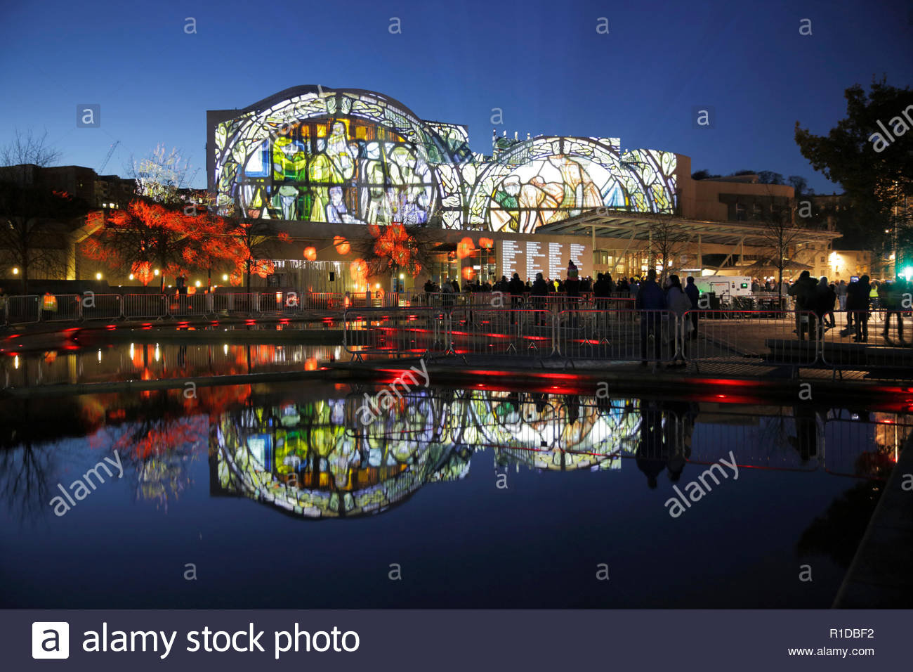 Edinburgh, United Kingdom. 11th November, 2018.  The Scottish Parliament building illuminated on Armistice day with images that tell the story of the world war 1 conflict alongside a Roll of Honour of those who died, reflected in the ornamental pond.   Credit: Craig Brown/Alamy Live News. Stock Photo