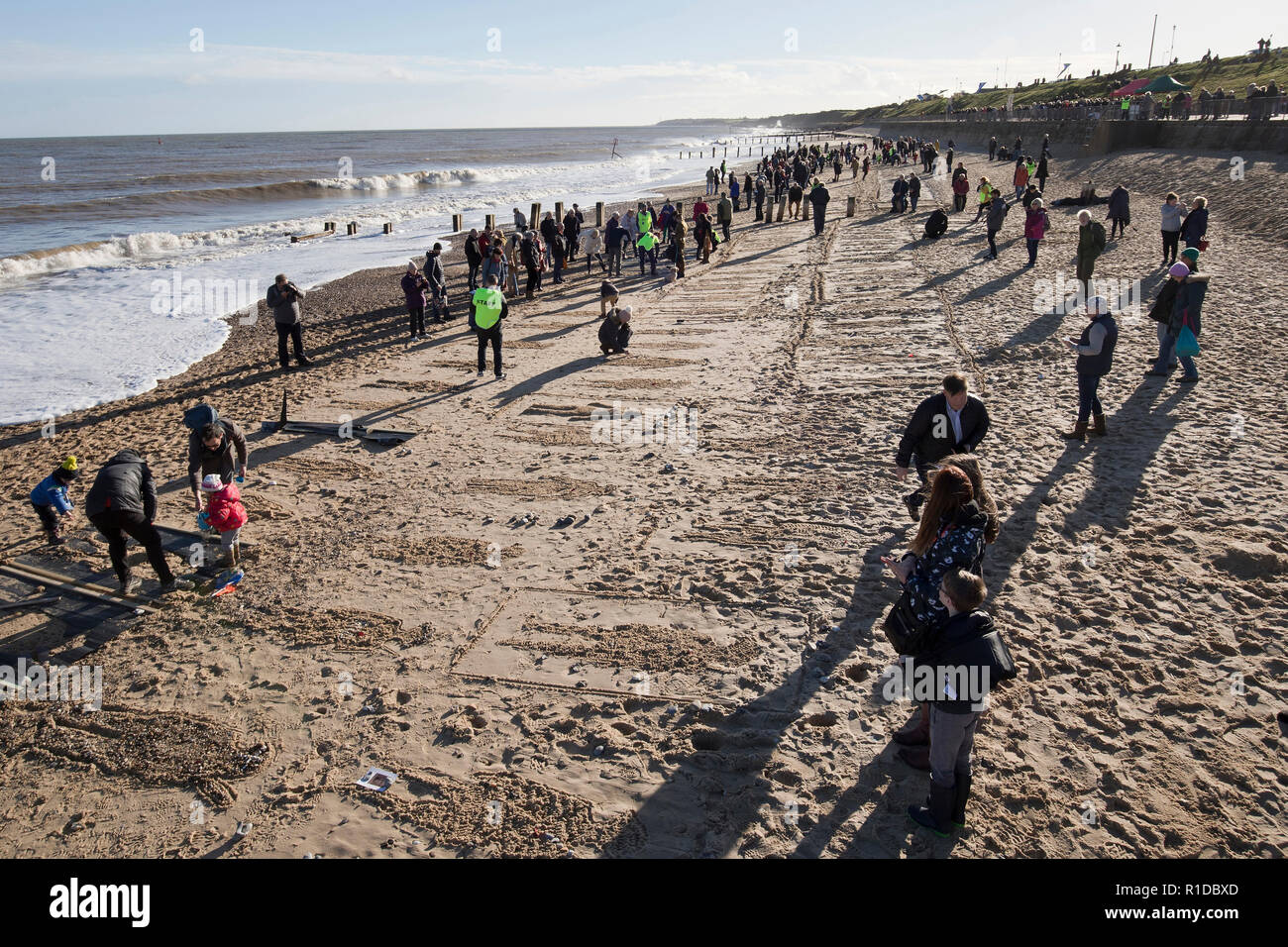 Gorleston-On-Sea, Norfolk. 11th November 2018. Crowds gather on Gorleston beach to participate in Danny Boyle's nationwide 'Pages of the Sea' commemoration, marking the end of the first world war 100 years ago, many making their own artistic contributions in the sand in remembrance of those individuals who left our shores and never returned. Credit: Adrian Buck/Alamy Live News Stock Photo