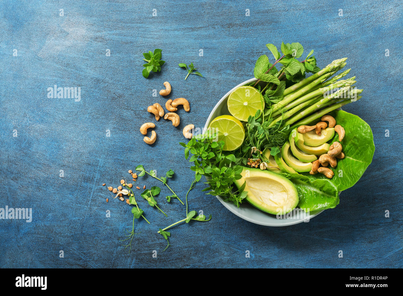 A bowl with a variety of herbs, avocados, asparagus, micro greens, lime and cashews. Detox bowl buddha. Blue rustic background, top view. Clean, whole Stock Photo