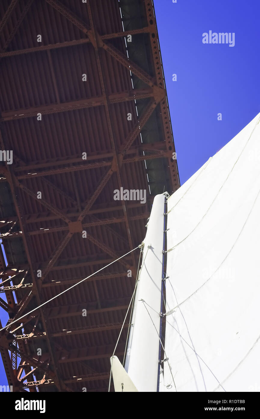 Detail of a sailboat mainsail underneath the GoldenGate Bridge with a