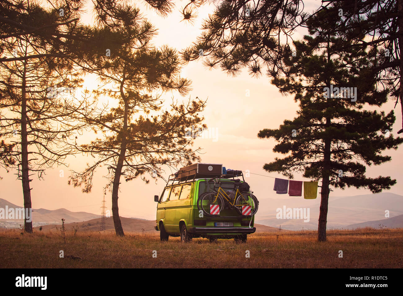 Old timer camper van parked on the top of the hill between pine trees in the beautiful sunset sky Stock Photo