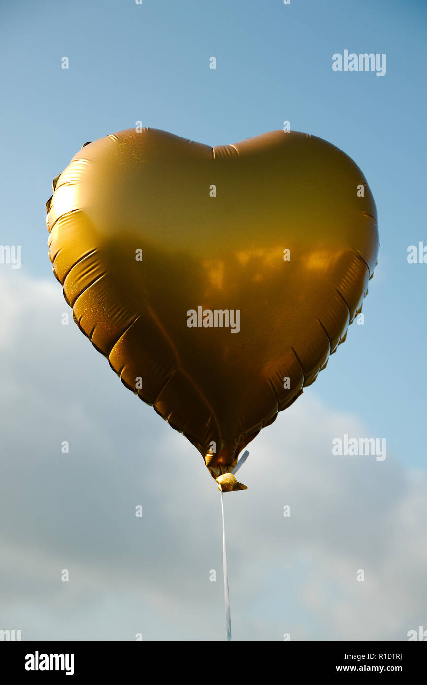 A gold heart shaped balloon flying against a blue sky background Stock ...