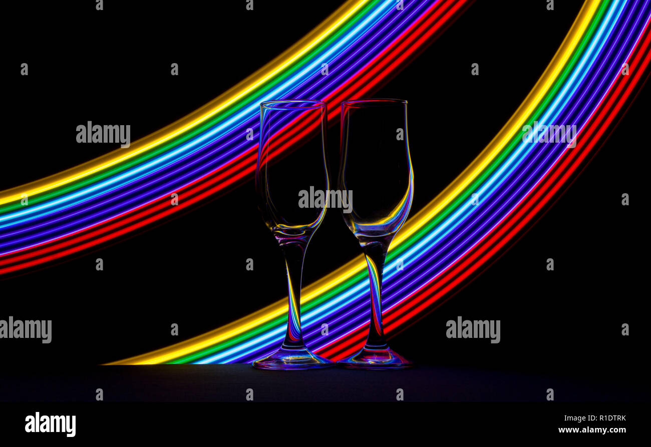 Two champagne glasses with streaks of multicoloured neon light behind