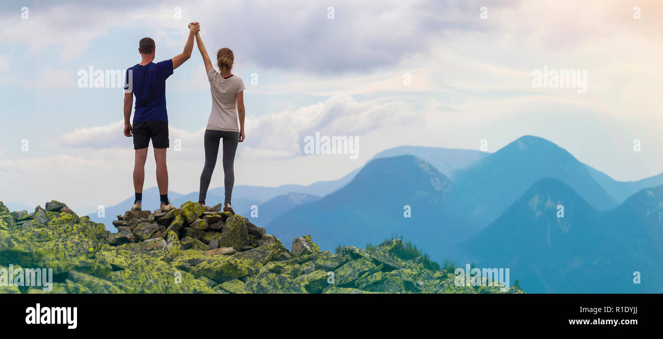 Back view of young tourist couple, athletic man and slim girl standing with  raised arms holding hands on rocky mountain top enjoying fantastic panoram  Stock Photo - Alamy