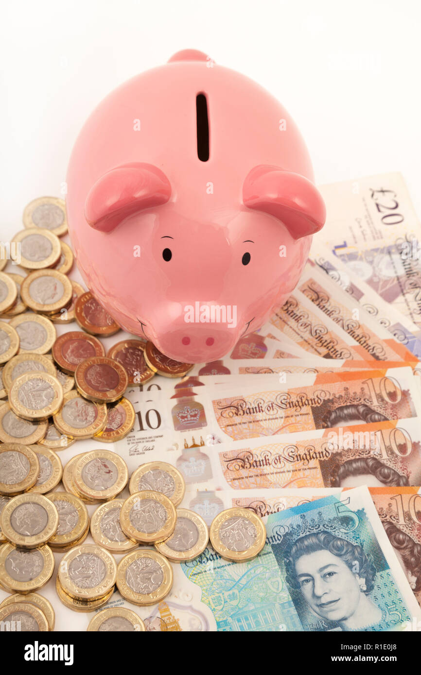 Pink Piggy bank on lots of pound notes and pound coins Stock Photo
