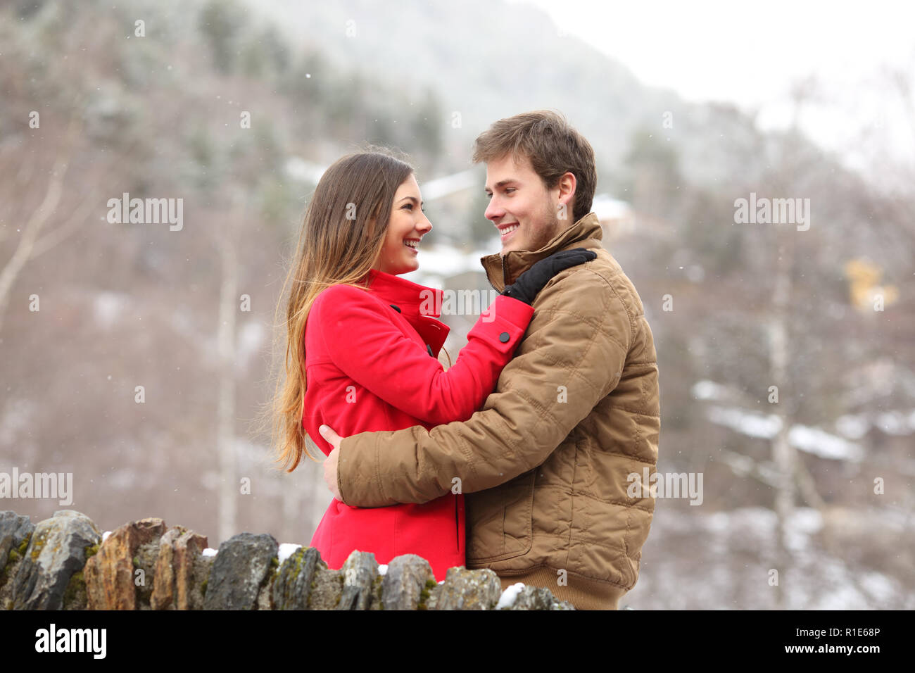 Happy couple hugging looking each other in winter holiday on a stone bridge in the mountain Stock Photo