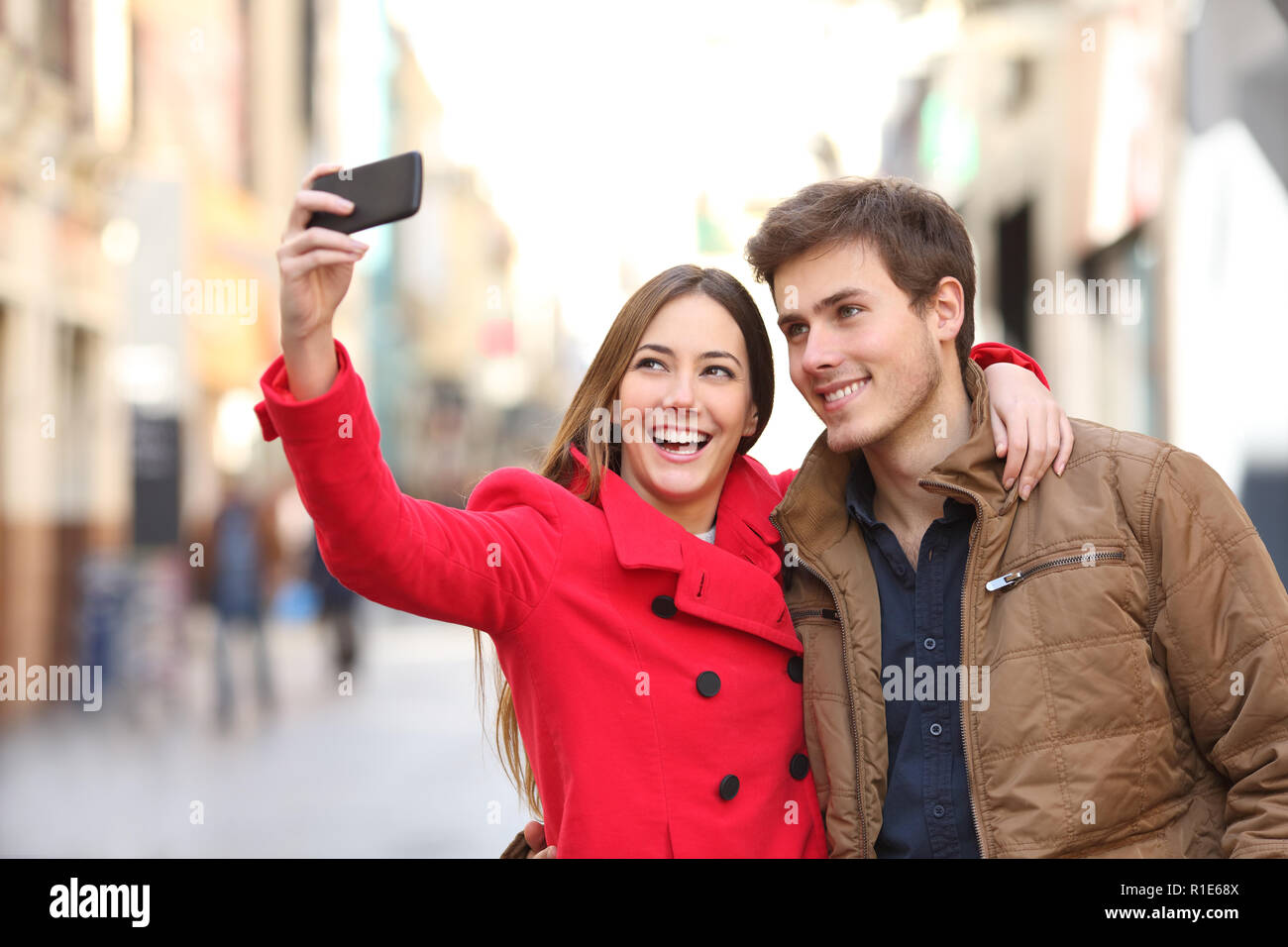 Happy couple taking selfies with a smart phone in the street in winter Stock Photo