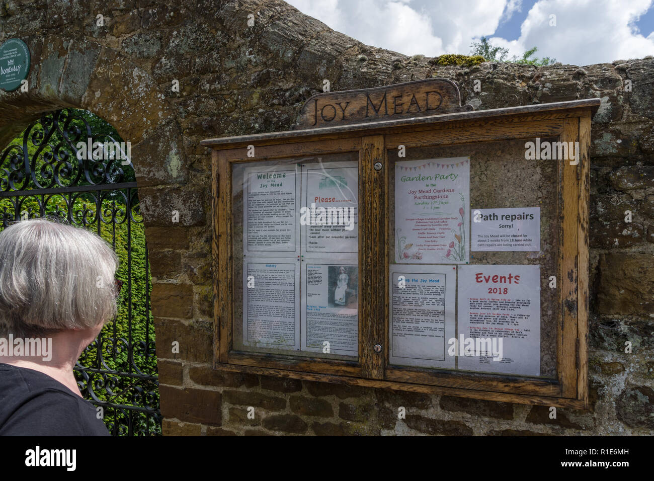 Senior woman reading the information board for Joy Mead Gardens in the village of Farthingstone, Northamptonshire, UK Stock Photo