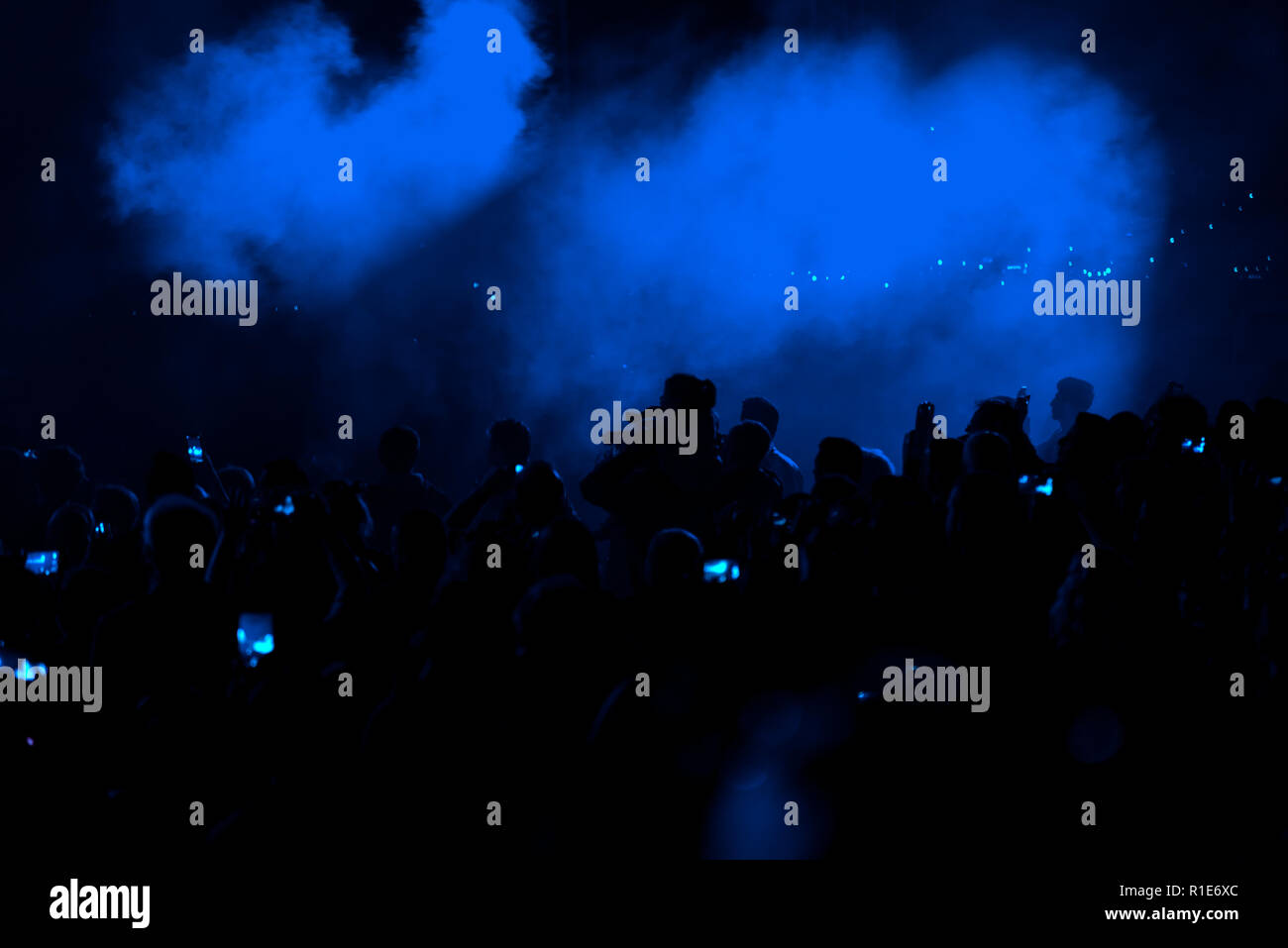 Concert field, crowded people and blue stage lights with smoke. Stock Photo