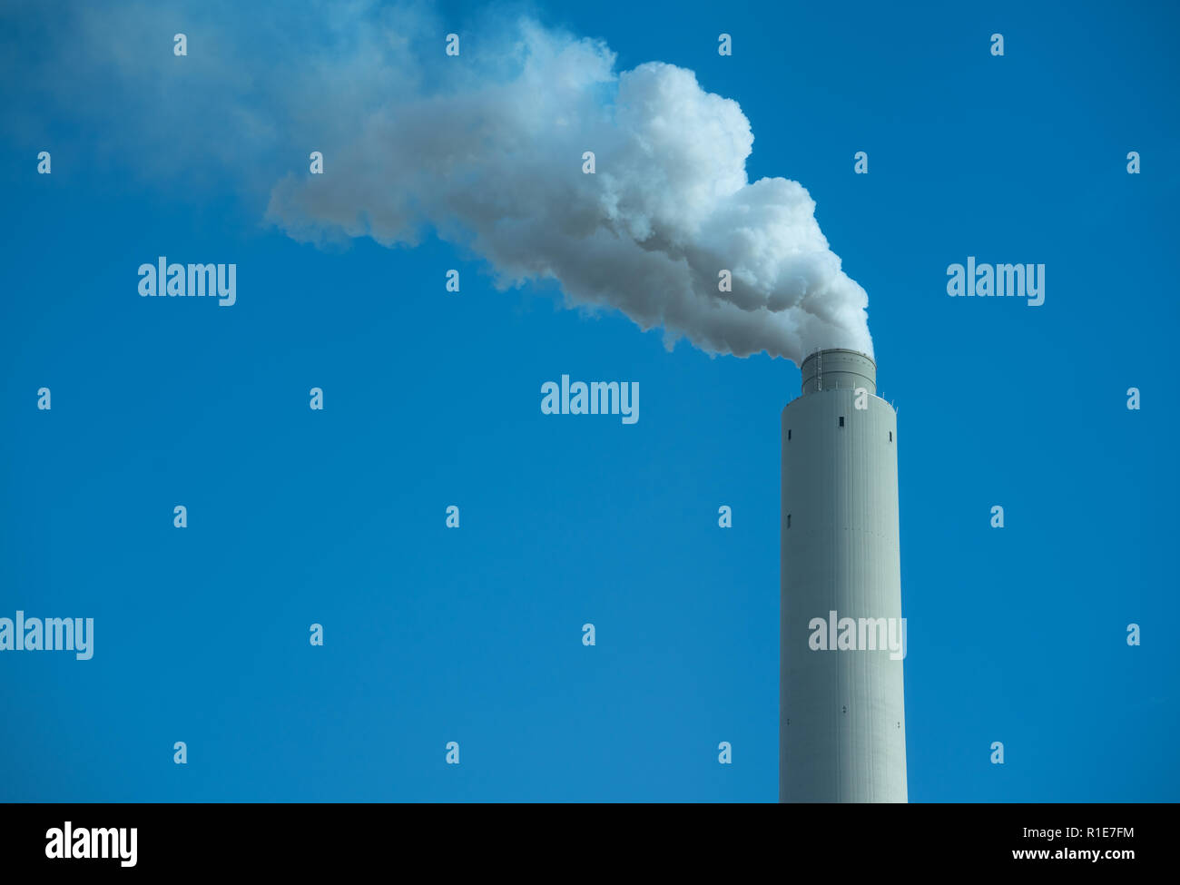 Smoke stack white smoke against blue sky landscape orientation with negative space. Stock Photo