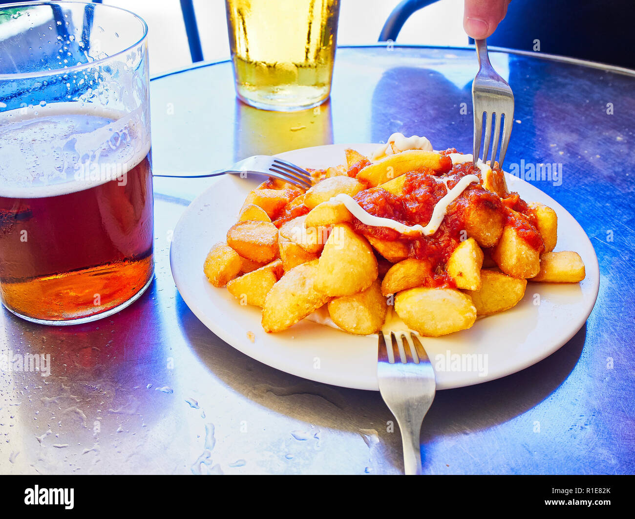 A portion of Patatas Bravas over a metallic table. Fried potatoes topped with spicy sauce, one of the most common typical Spanish tapas. Stock Photo