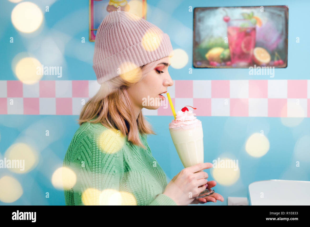 Portrait of a lovely girl in green sweater with bokeh lights. Pretty blonde girl with a milkshake Stock Photo