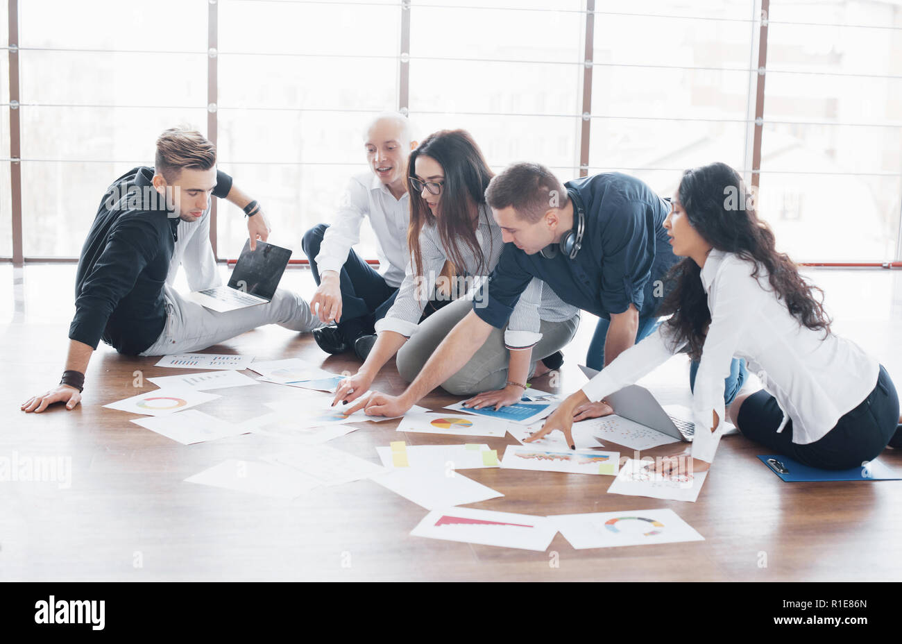 Young creative people in modern office. Group of young business people are working together with laptop. Freelancers sitting on the floor. Cooperation corporate achievement. Teamwork concept Stock Photo