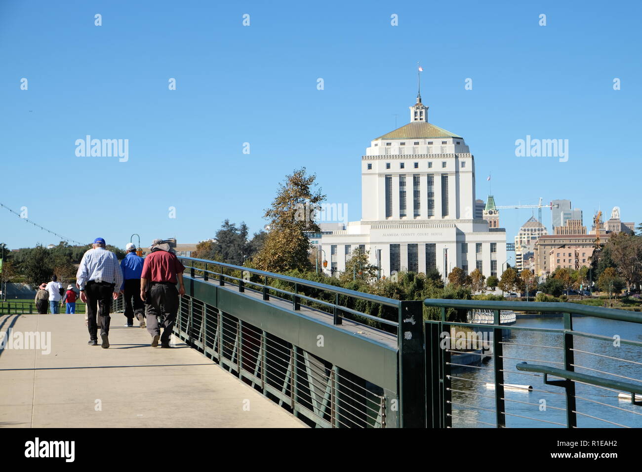 Alameda County Court House and Lake Merritt, Oakland, California, USA; pedestrian bridge with people walking. Stock Photo