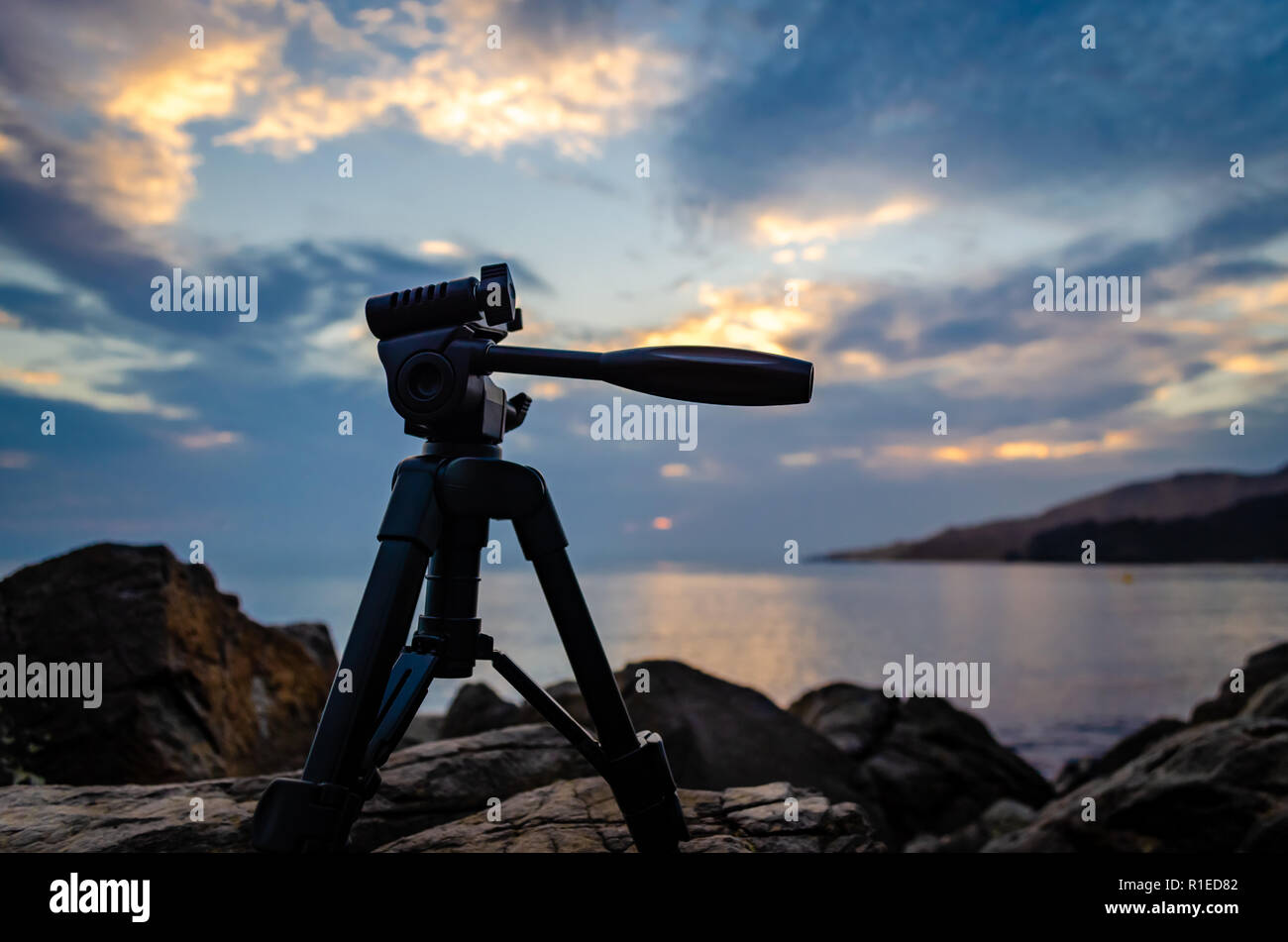Low key shot of a tripod placed on rocks during sunrise. Stock Photo